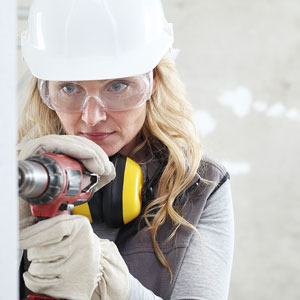 safety-conscious carpenter wearing safety glasses and gloves while drilling a hole in sheetrock